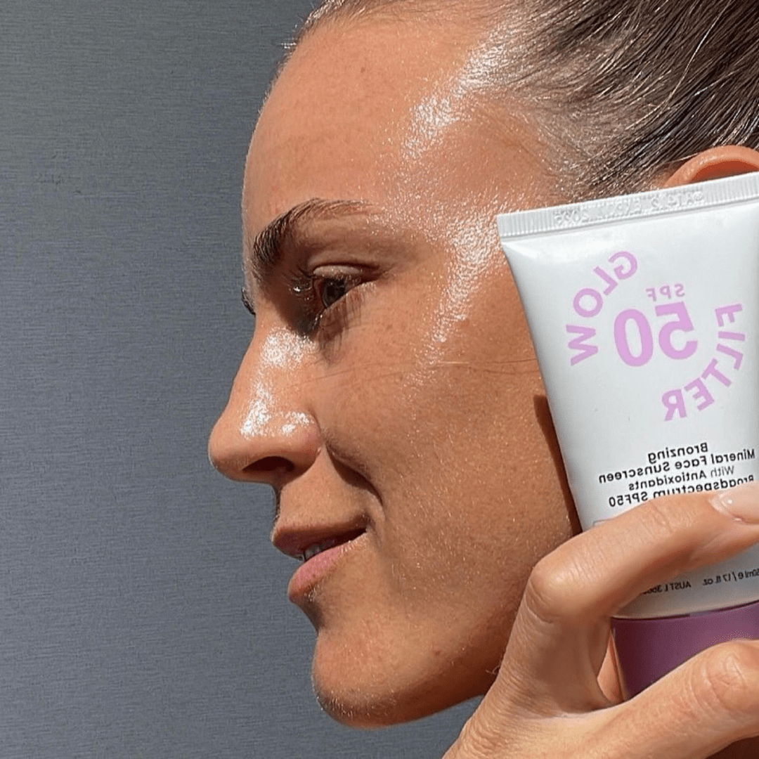 Woman holding SS SPF 50 Glow Filter Bronzing Mineral Sunscreen, close-up shot showing glowing skin.