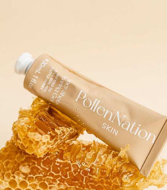 An elegantly presented tube of Pollen Nation Skin face moisturiser, resting on a piece of natural honeycomb against a cream-colored background. The honeycomb is oozing honey, evoking the natural ingredients used in the beauty product. This image highlights the organic and nature-inspired ethos of the Australian skincare brand.