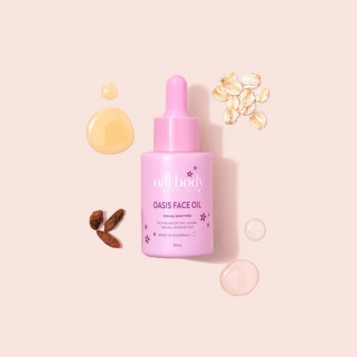 Oatbody Oasis Face Oil in a pink bottle with dropper, accompanied by drops of yellow oil, oat flakes, and almond pieces on a soft pink background, emphasizing the product's natural ingredients and benefits for all skin types.