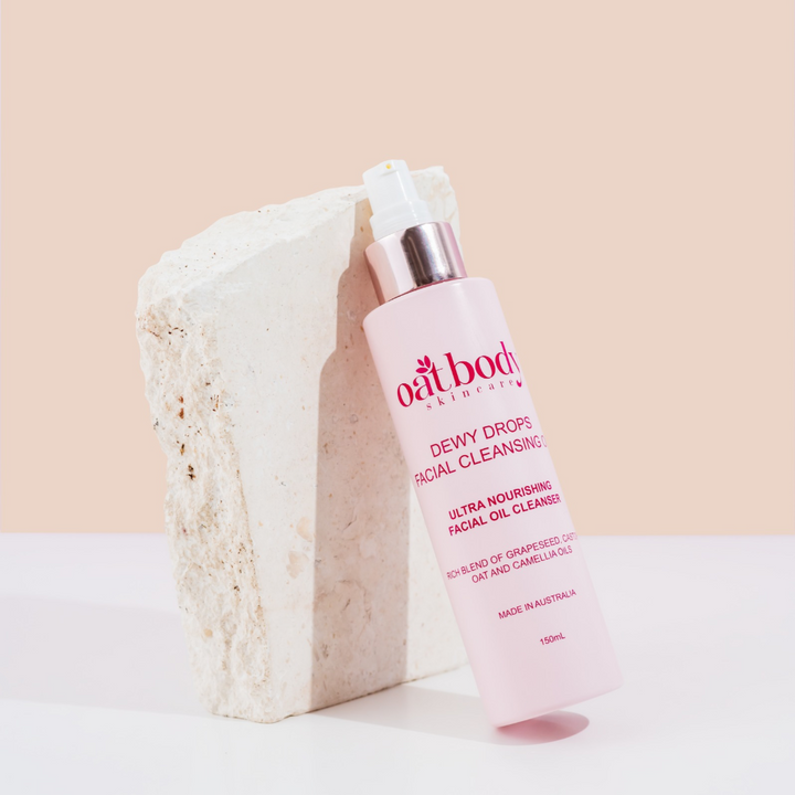 Oatbody Dewy Drops Facial Cleansing Oil bottle resting against a natural stone, showcasing its ultra-nourishing blend of oils for sensitive skin.