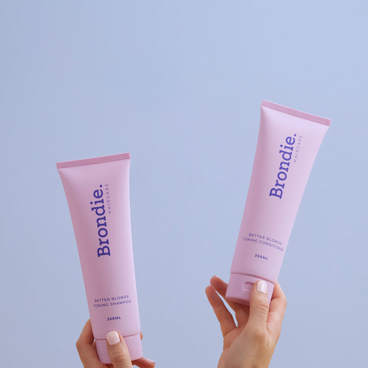 Hand holding Brondie Haircare's Better Blonde toning shampoo tube and blonde toning conditioner for toning blonde hair in Australia.
