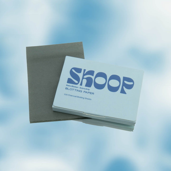 Skoop Babe Blotter Extra Drip Charcoal Blotting Paper, featuring 100 charcoal-infused sheets displayed with its sleek light blue packaging. Perfect for absorbing excess oil and purifying skin, the blotting papers are showcased against a dreamy sky background, highlighting their fresh and natural appeal.