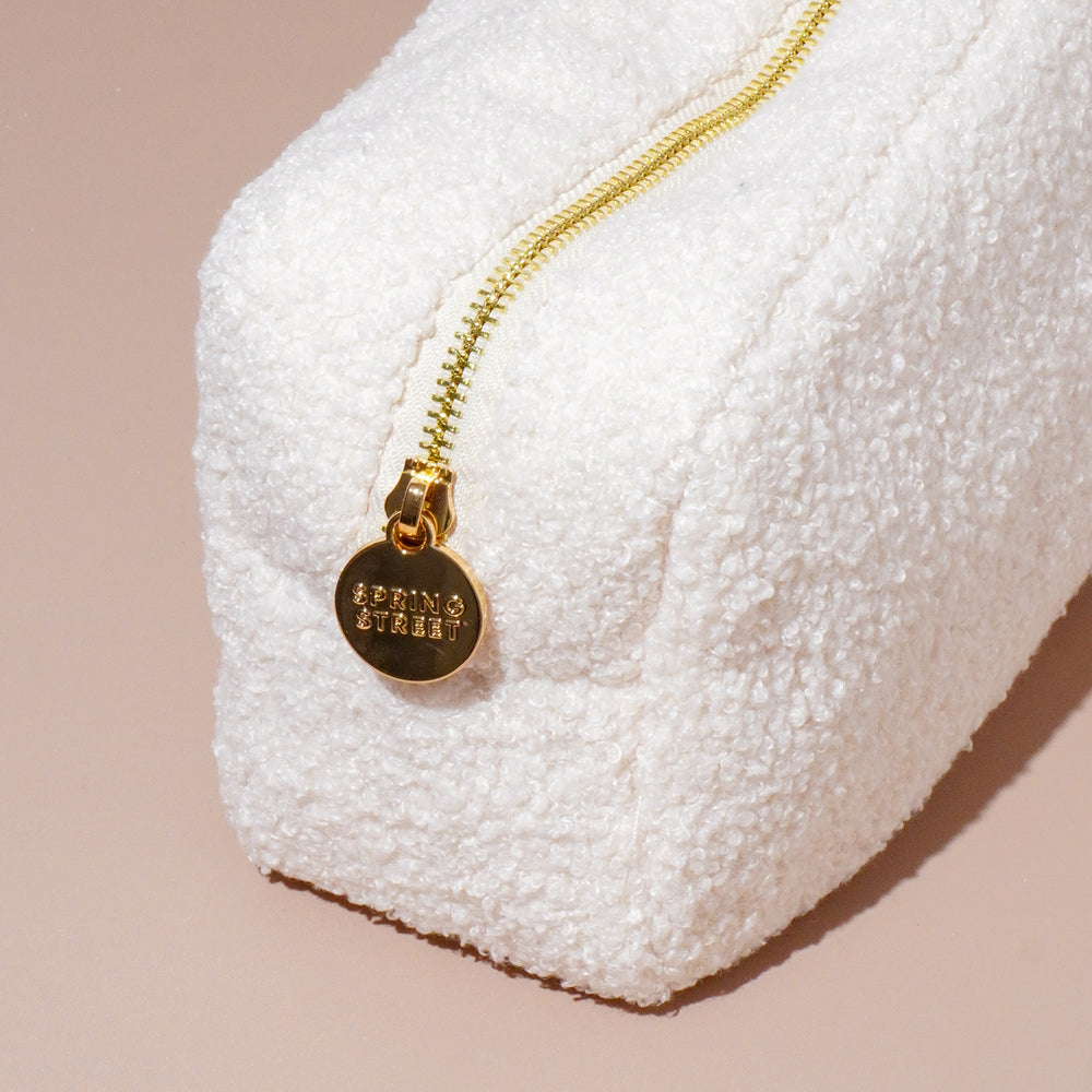 Close-up of a white teddy cosmetic bag with a gold zipper and 'Spring Street' branded charm, highlighting its soft, plush texture and elegant design.