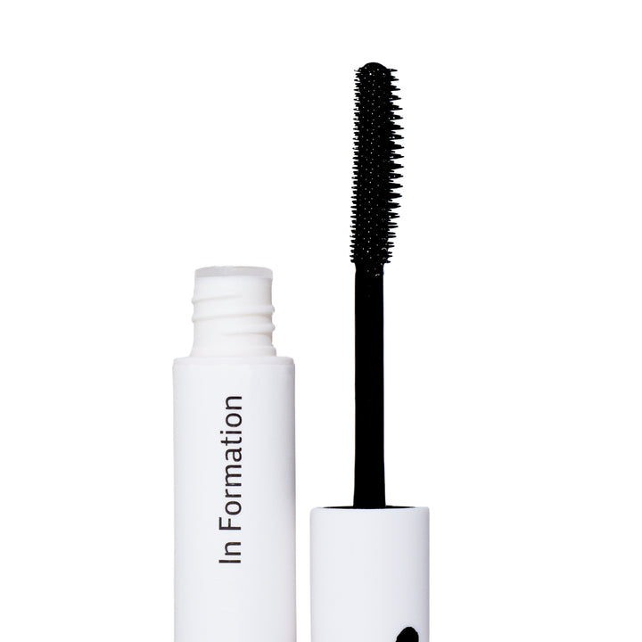 The image shows an open white cylindrical bottle labeled "In Formation. Next to the bottle is an applicator best flyaway products with a black wand and a spiral-bristled brush that is coated with a product, this is a hair tool. This product is for hair care, designed to tame flyaways and tame frizzy hair —this is supported by the wand's resemblance to a mascara applicator.