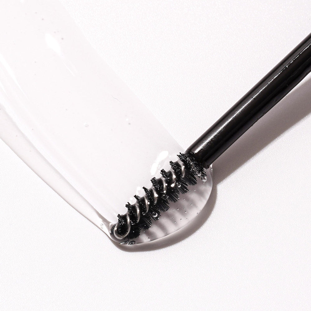 Close-up of a spoolie brush with clear eyebrow gel, showing the texture and consistency of the gel on a white background.