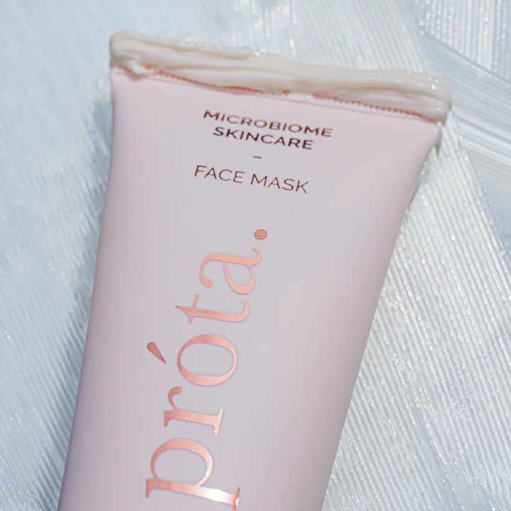 Close-up of an open tube of Prōta Microbiome Skincare Face Mask, showing the creamy product texture oozing out, set against a textured white background to emphasize the product’s rich formula.