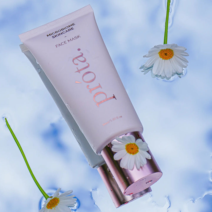 Microbiome Skincare Face Mask tube in a refreshing setting with water droplets and floating daisies against a cloudy sky backdrop, highlighting the product's hydrating and soothing properties.