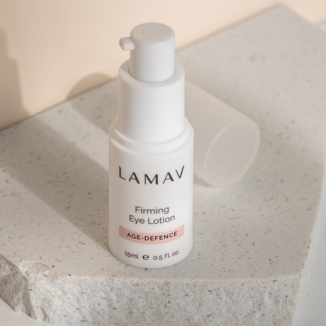 Bottle of LAMAV Organic Firming Eye Lotion, part of the AGE-DEFENCE line, 15ml. The product is presented in a sleek, white dispenser with clear labeling, designed for reducing the appearance of fine lines around the eyes.