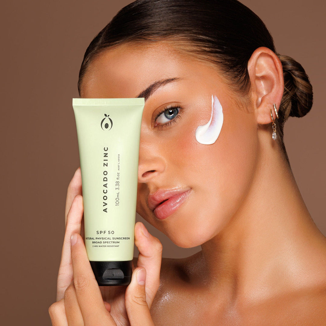 Model holding Avocado Zinc SPF 50 Natural Physical Sunscreen from VAMS Beauty, with a swatch of the sunscreen on her cheek. This Australian-made sunscreen offers broad-spectrum protection, is water-resistant, and ideal for sensitive skin, providing effective sun protection with a smooth, non-greasy formula.