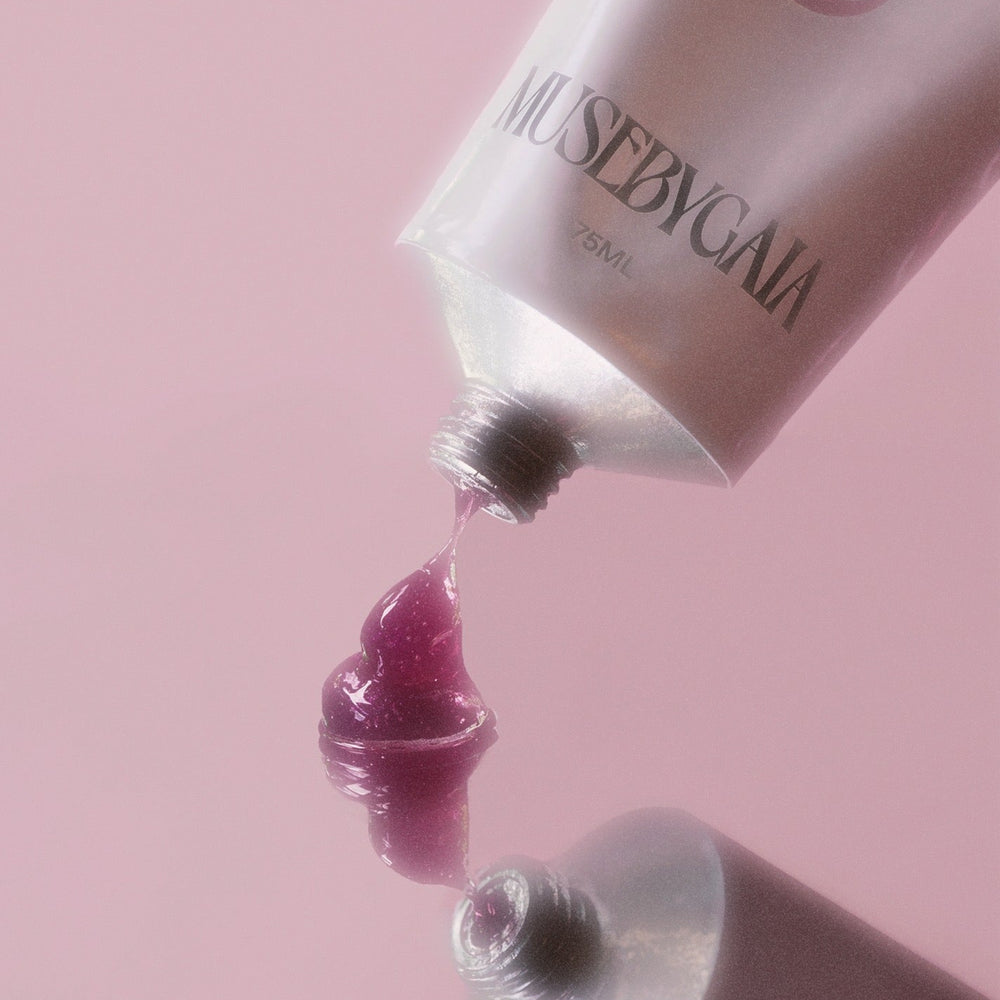 Pink jelly exfoliant pouring from a Muse by Gaia tube against a soft pink background, highlighting the smooth texture and vibrant color of the skincare product.