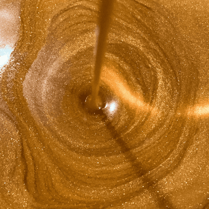 Close-up of shimmering golden body oil being poured, highlighting its rich, luxurious texture designed to enhance skin with a radiant glow