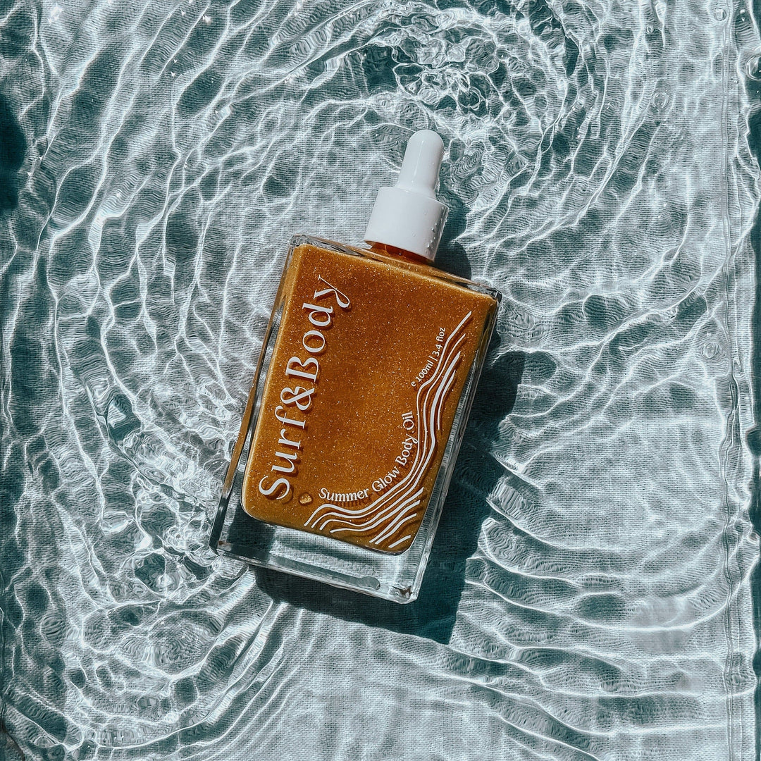 Surf & Body Summer Glow Body Oil bottle floating on shimmering water, highlighting its golden, radiant formula designed to enhance the skin with a sun-kissed glow.