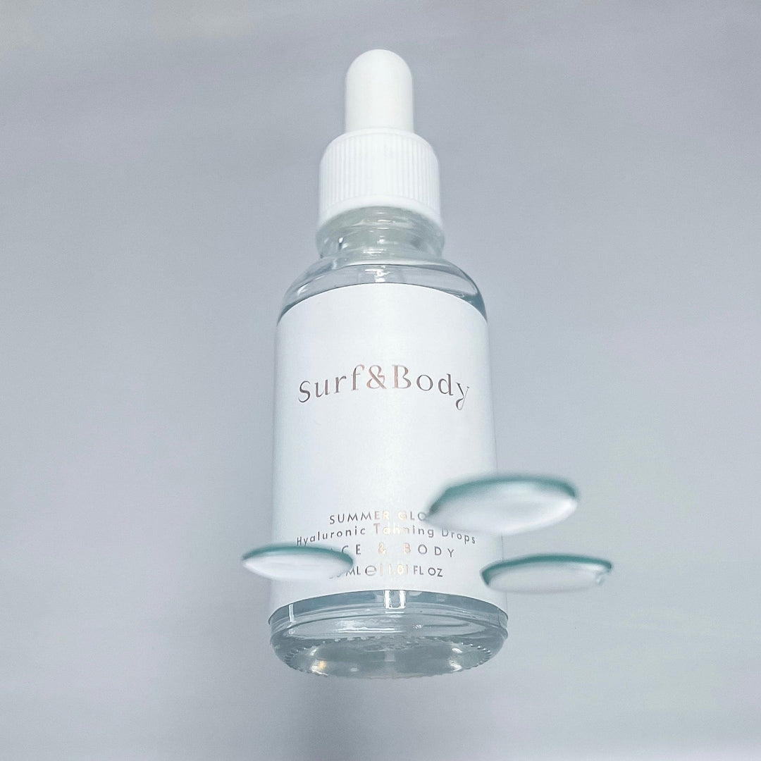 Surf & Body Summer Glow Hyaluronic Tanning Drops bottle with water droplets, showcasing the hydrating and lightweight nature of the product.