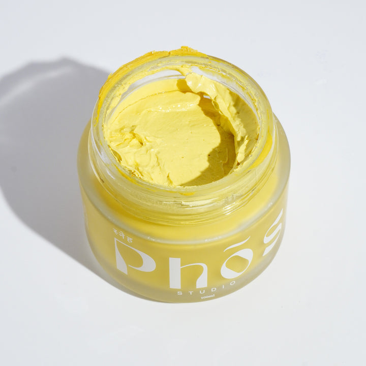 Open jar of Phos Studio Turmeric & Neem Face Mask with 5% AHA Fruit Acids, showcasing the vibrant yellow, creamy texture of the Ayurvedic-inspired skincare product, designed to detoxify, brighten, and hydrate the skin.